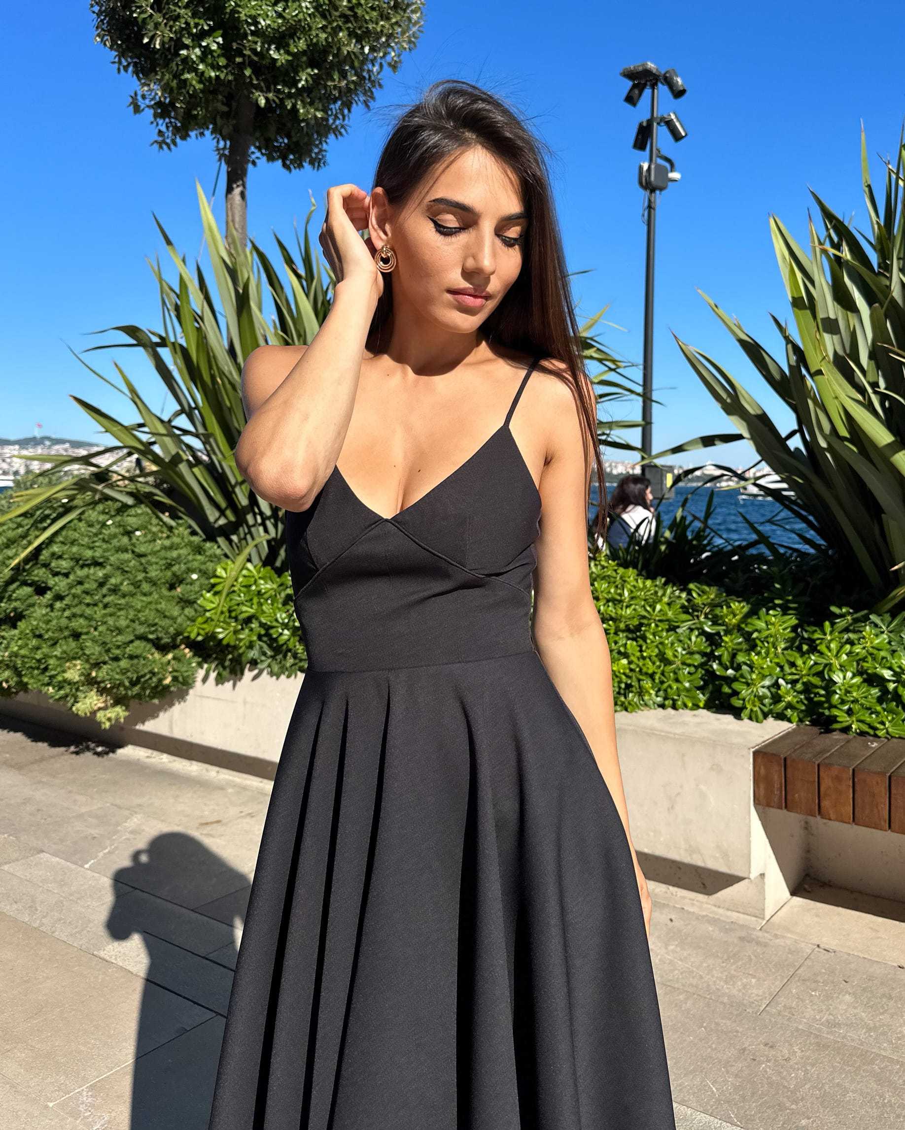 Rochie neagra eleganta scurta cu bretele, fusta evazata, femeie imbracata, fundal natural.