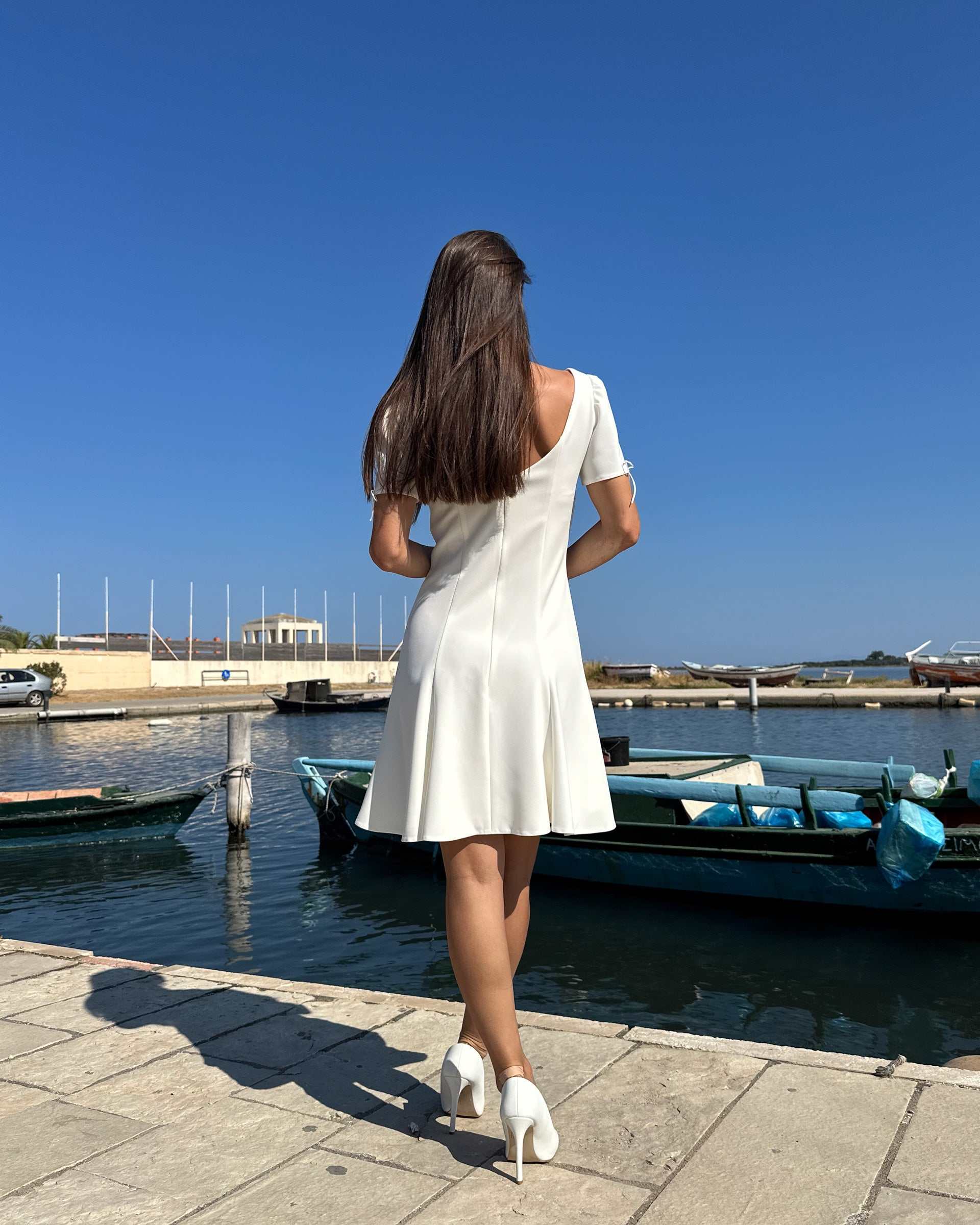 Rochie albă scurtă cloș cu mâneci, din stofă semielastică, purtată lângă apă.