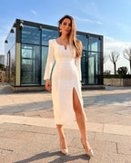Rochie albă elegantă cu mâneci lungi și slit pe piciorul stâng, perfectă pentru evenimente speciale.