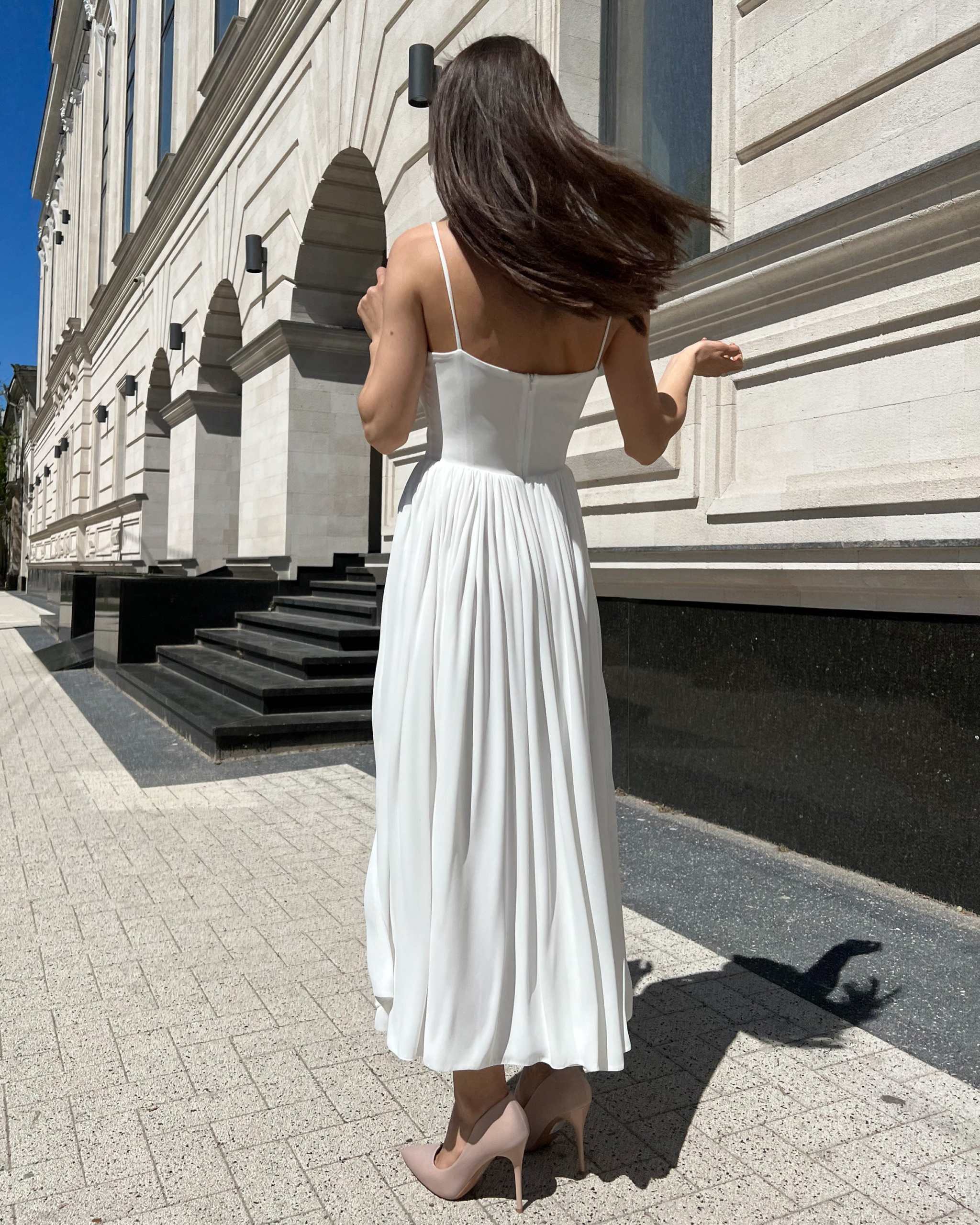 Rochie alba elegantă cu bretele și slit, lungime midi, accesorizată cu centură.