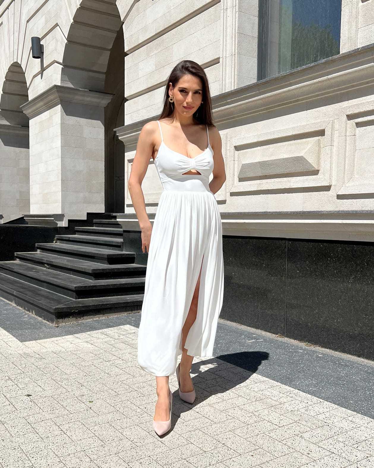 Rochie alba elegantă midi cu bretele și slit, accesorizată cu centură.