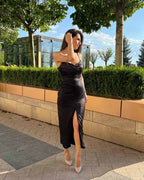 Rochie cocktail neagră de seară din satin elastic cu tăietură centrală și pliuri, purtată de un model.